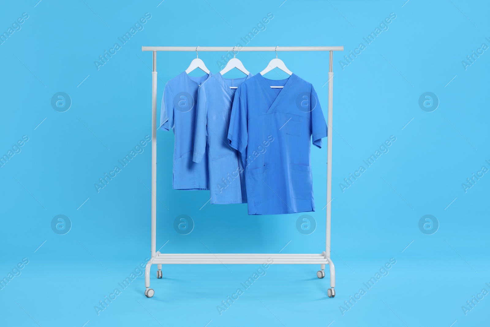 Photo of Medical uniforms on rack against light blue background