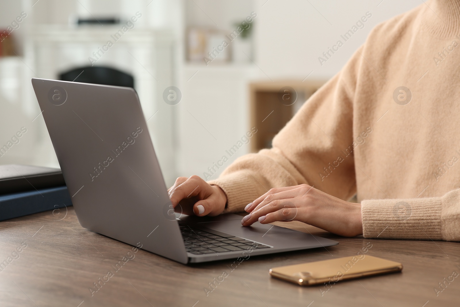 Photo of Woman working with laptop at wooden desk indoors, closeup