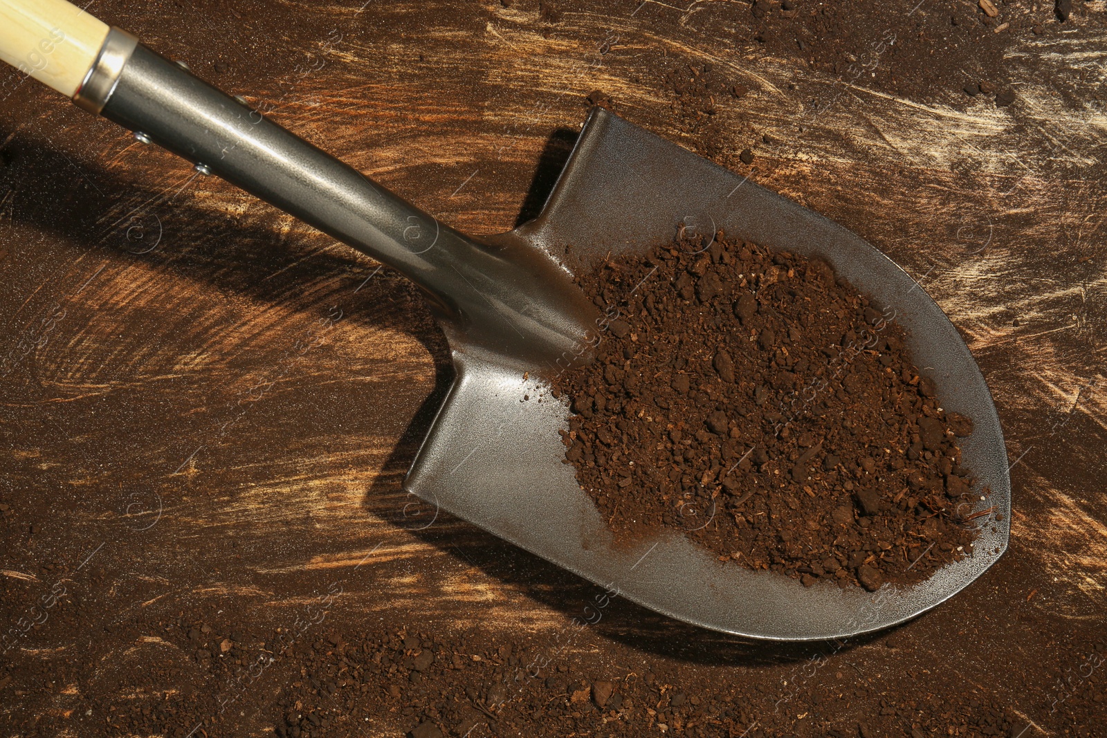 Metal shovel with fertile soil on dirty wooden surface, top view Photo of Metal shovel with fertile soil on dirty wooden surface, top view