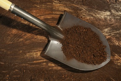 Photo of Metal shovel with fertile soil on dirty wooden surface, top view