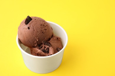 Photo of Cup with tasty chocolate ice cream on yellow background. Space for text