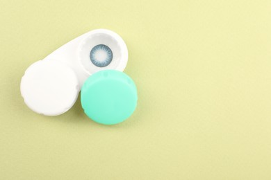 Photo of Case with blue contact lenses on light green background, top view. Space for text