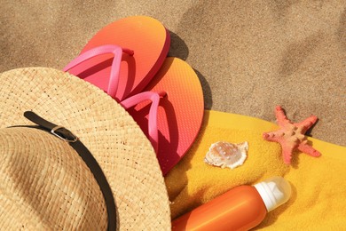 Photo of Straw hat, flip flops and other beach items on sand, flat lay