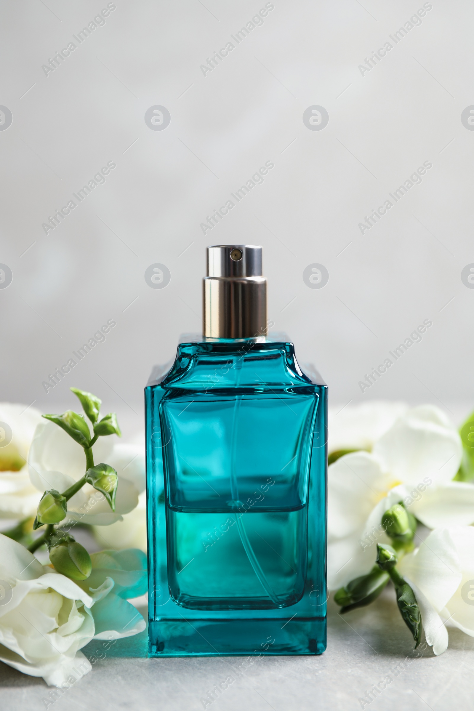 Photo of Bottle of perfume and beautiful flowers on light table