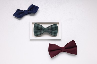 Photo of Stylish color bow ties on white textured background, flat lay