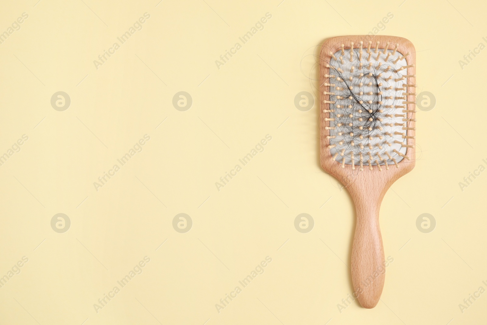 Photo of Wooden brush with lost hair on beige background, top view. Space for text