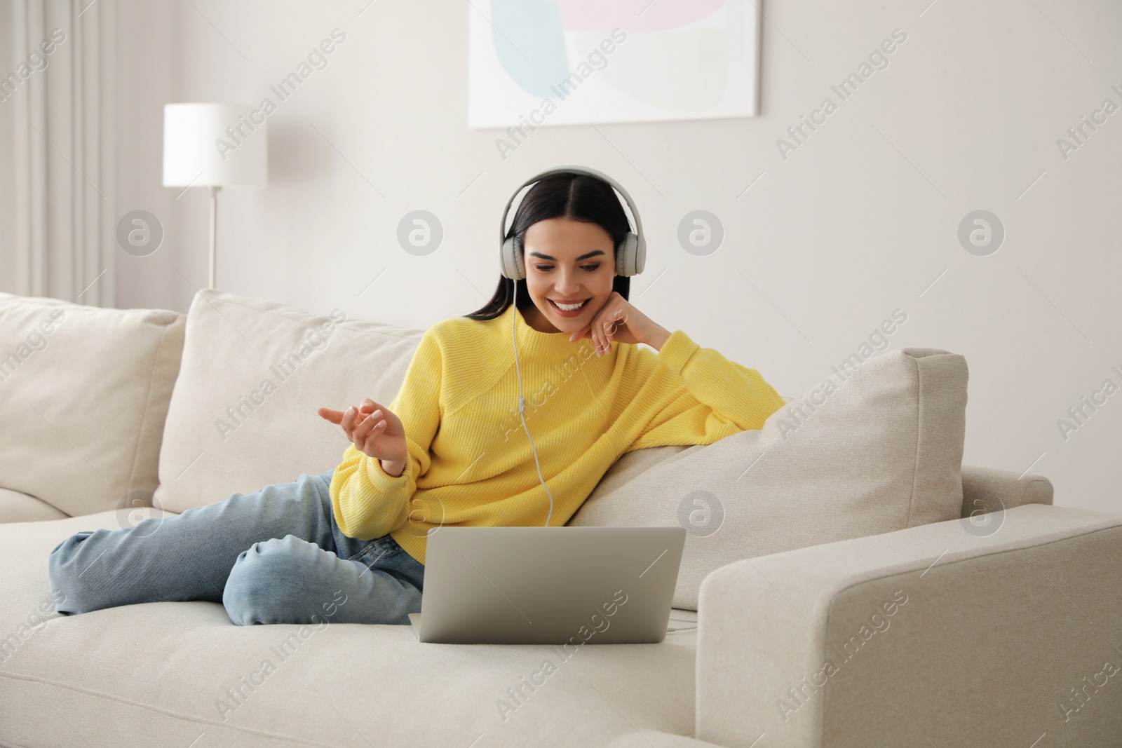 Photo of Woman with laptop and headphones sitting on sofa at home