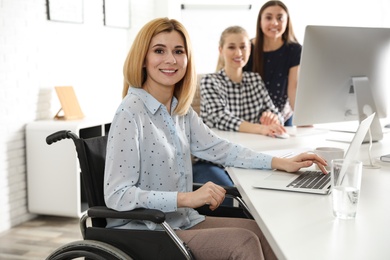 Portrait of woman in wheelchair with her colleagues at workplace