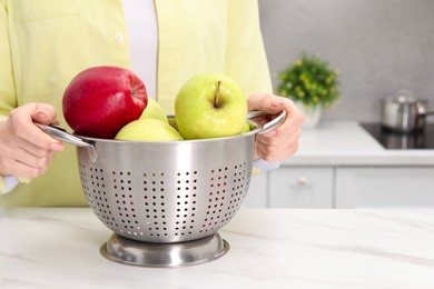 Photo of Woman holding colander with fresh apples at white marble table in kitchen, closeup. Space for text