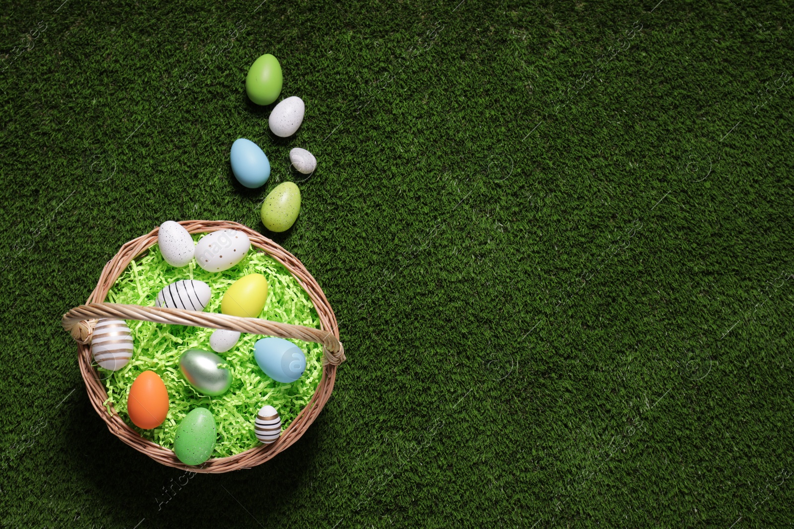 Photo of Easter basket and painted eggs on green grass, flat lay. Space for text