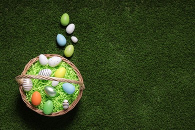 Photo of Easter basket and painted eggs on green grass, flat lay. Space for text