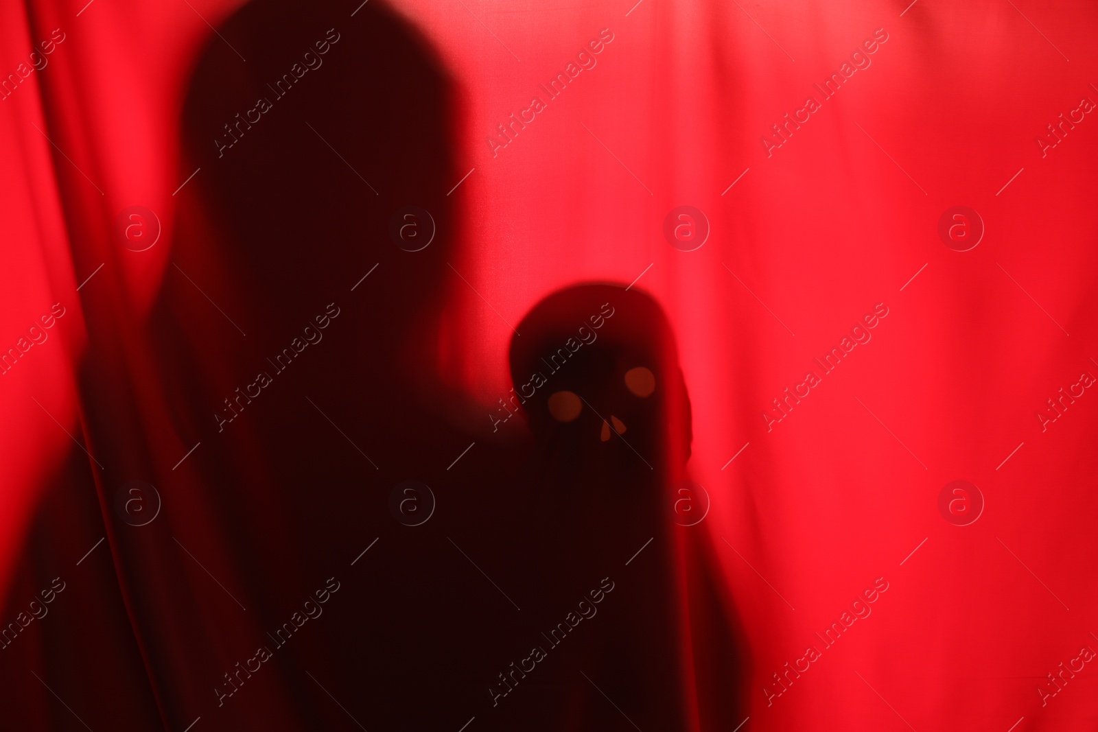 Photo of Silhouette of creepy ghost with skull behind red cloth, space for text