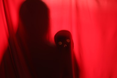 Silhouette of creepy ghost with skull behind red cloth, space for text