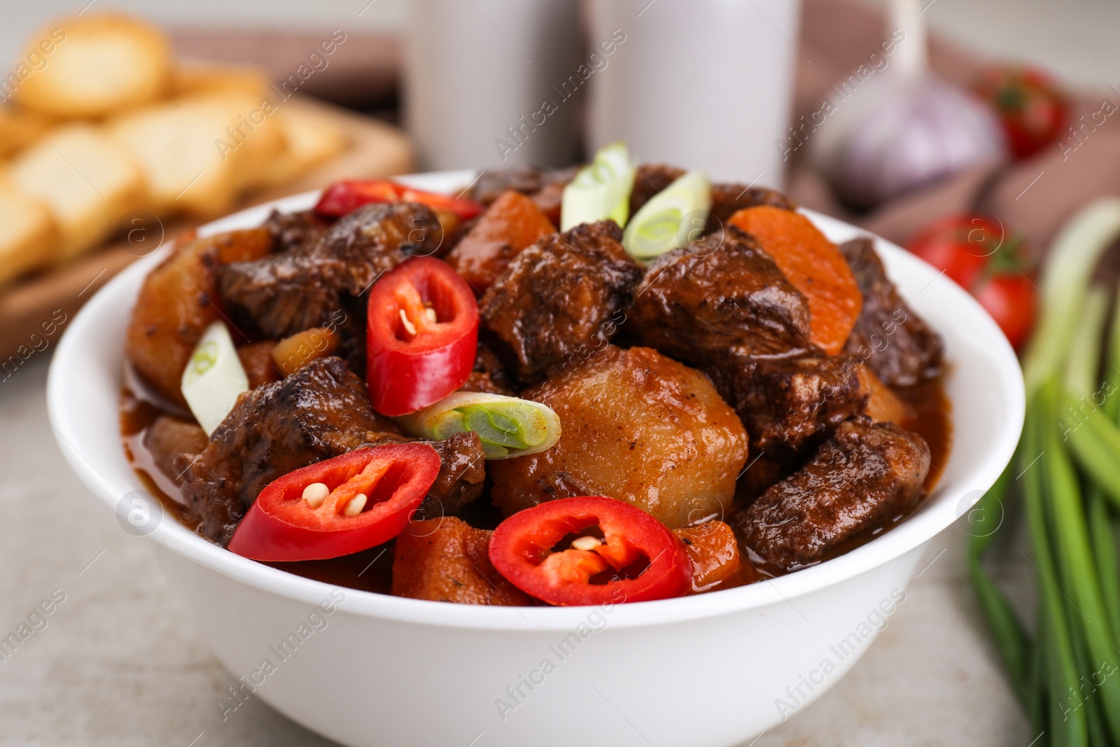 Photo of Delicious beef stew with carrots, chili peppers, green onions and potatoes on white textured table, closeup