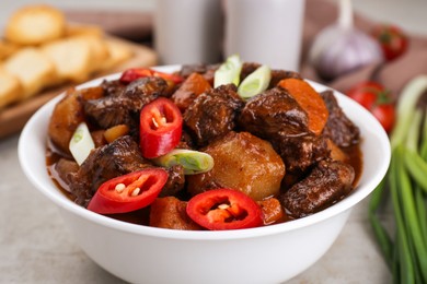 Delicious beef stew with carrots, chili peppers, green onions and potatoes on white textured table, closeup