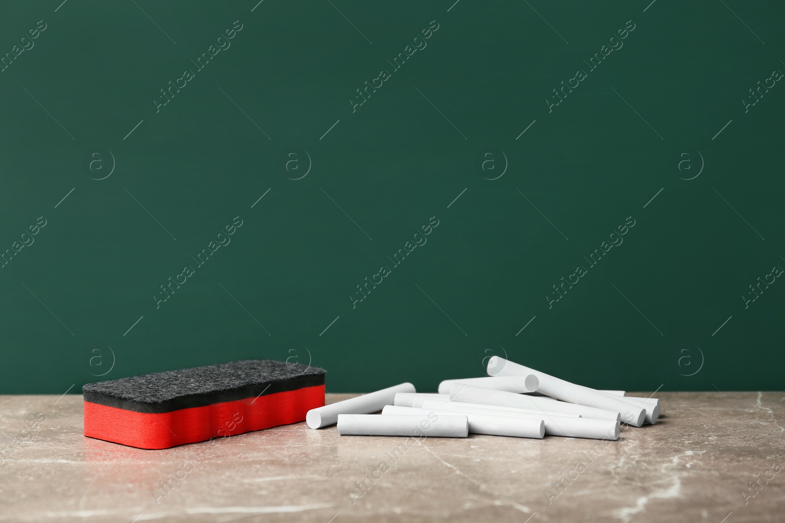 Photo of Pieces of chalk and duster on table near board