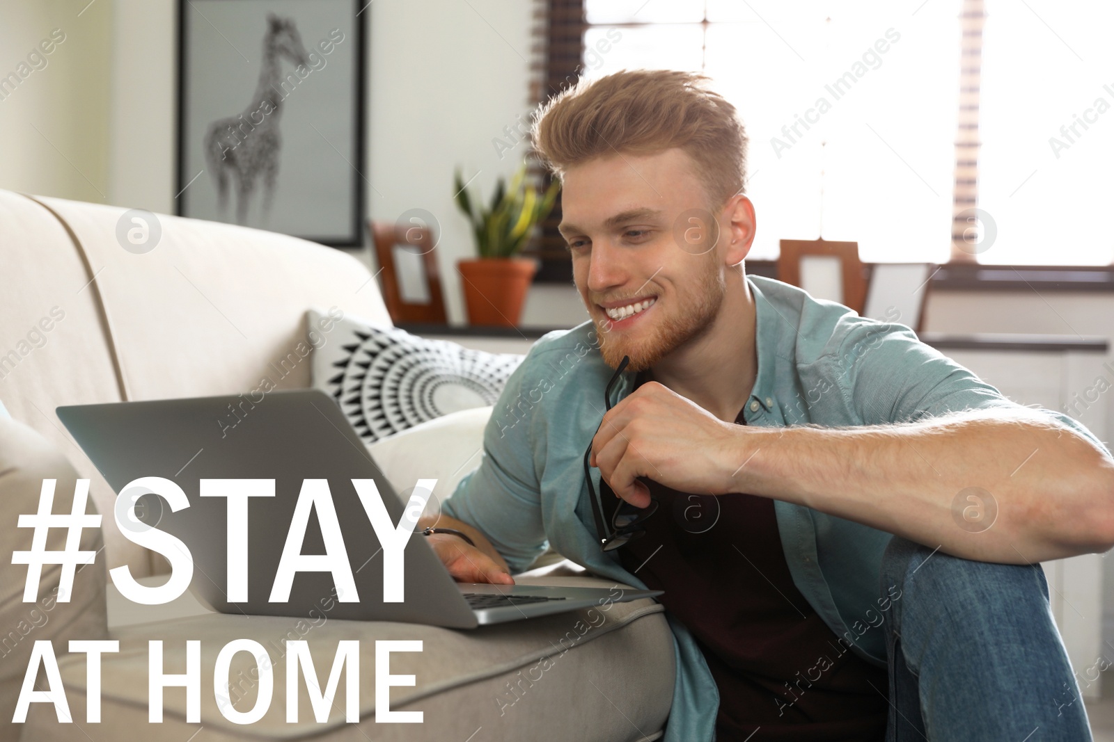 Image of Hashtag Stay At Home - protective measure during coronavirus pandemic. Young man working with laptop in living room