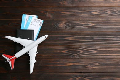 Toy airplane and passport with tickets on wooden background, flat lay. Space for text