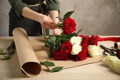 Photo of Woman making luxury bouquetfresh roses at wooden table, closeup