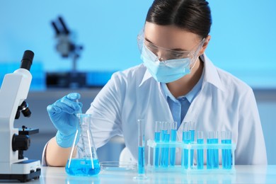 Photo of Scientist taking sample of light blue liquid and test tubes in laboratory