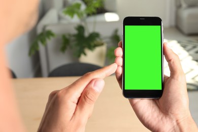 Chroma key compositing. Man using smartphone with green screen indoors, closeup. Mockup for design