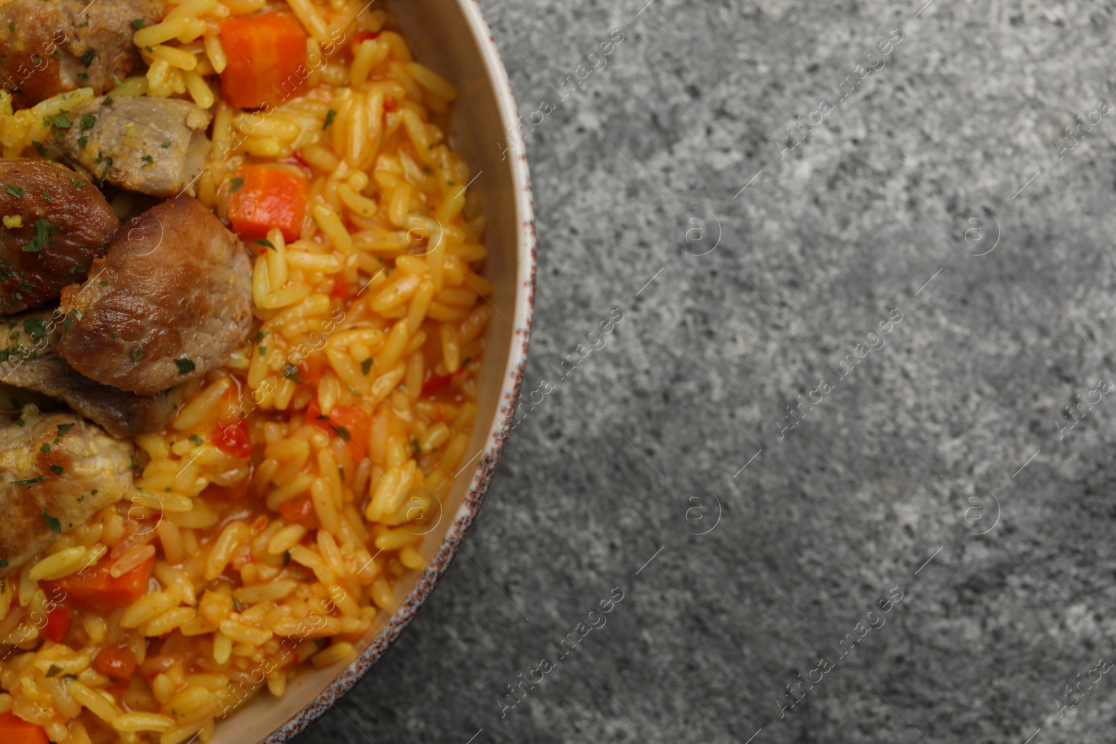 Photo of Delicious pilaf with meat on grey textured table, top view. Space for text