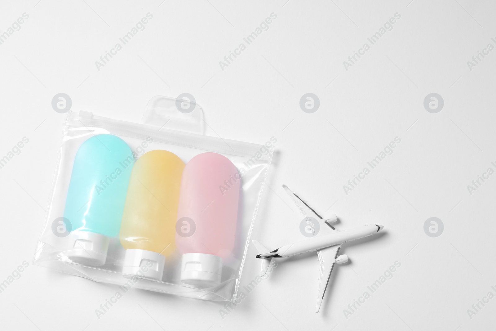 Photo of Cosmetic travel kit in plastic bag and toy plane on white background, top view with space for text. Bath accessories