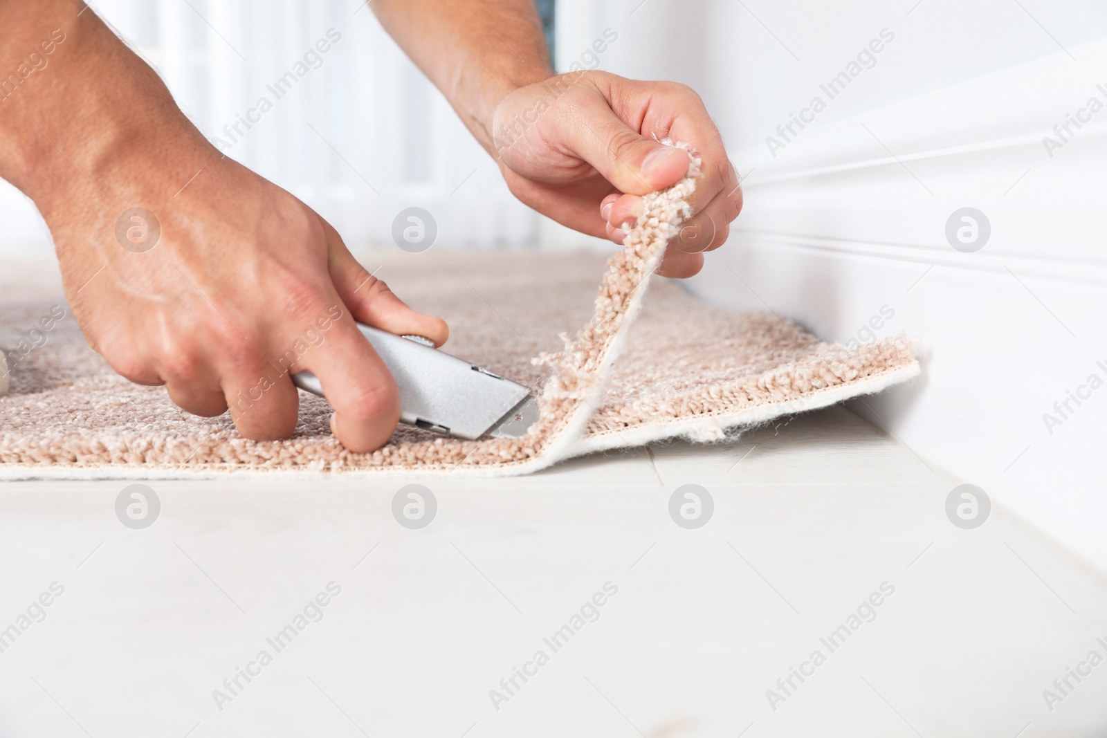 Photo of Man cutting new carpet flooring indoors, closeup. Space for text