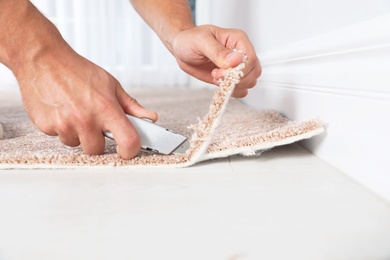 Photo of Man cutting new carpet flooring indoors, closeup. Space for text