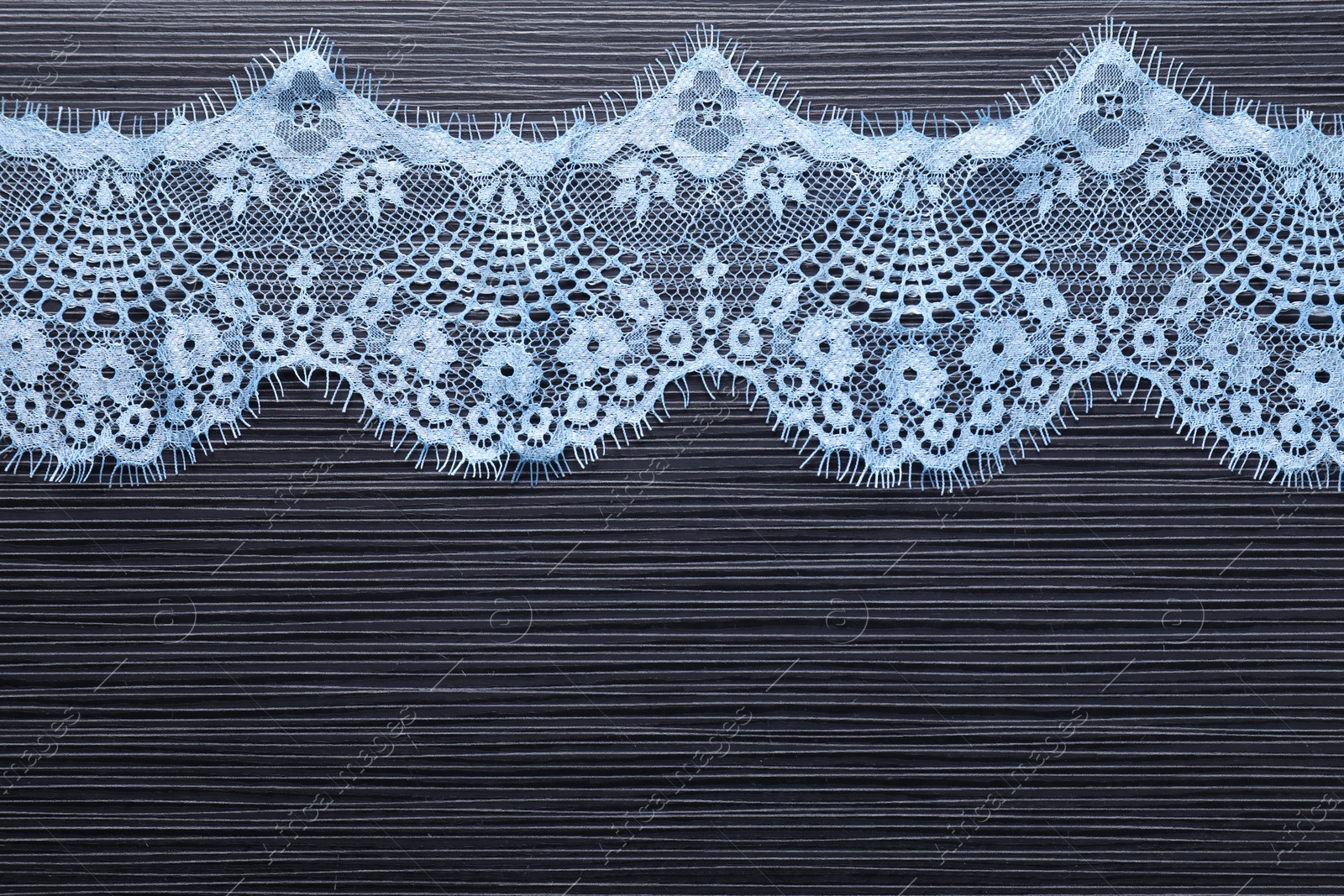 Photo of Light blue lace on black table, top view. Space for text