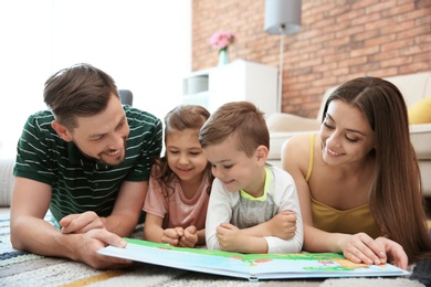 Photo of Young couple reading book with children at home. Happy family