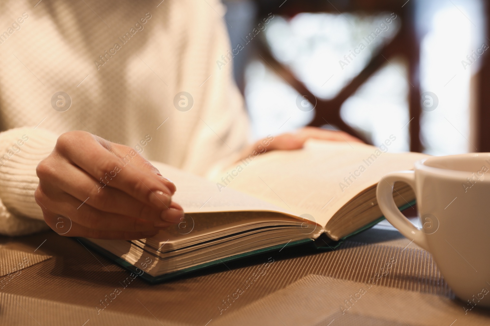 Photo of Woman with coffee reading book at wooden table, closeup