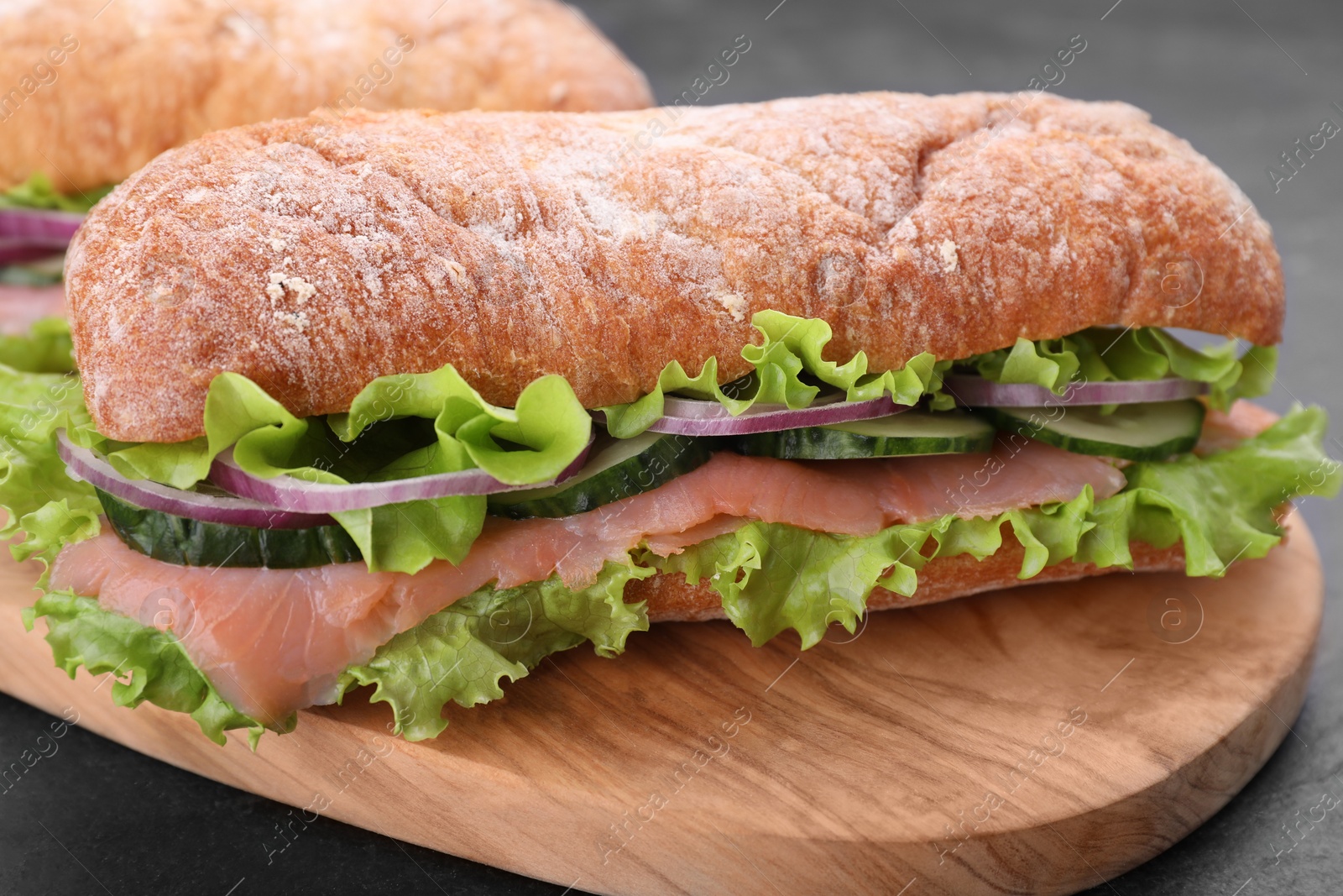 Photo of Delicious sandwich with fresh vegetables and salmon on wooden board, closeup