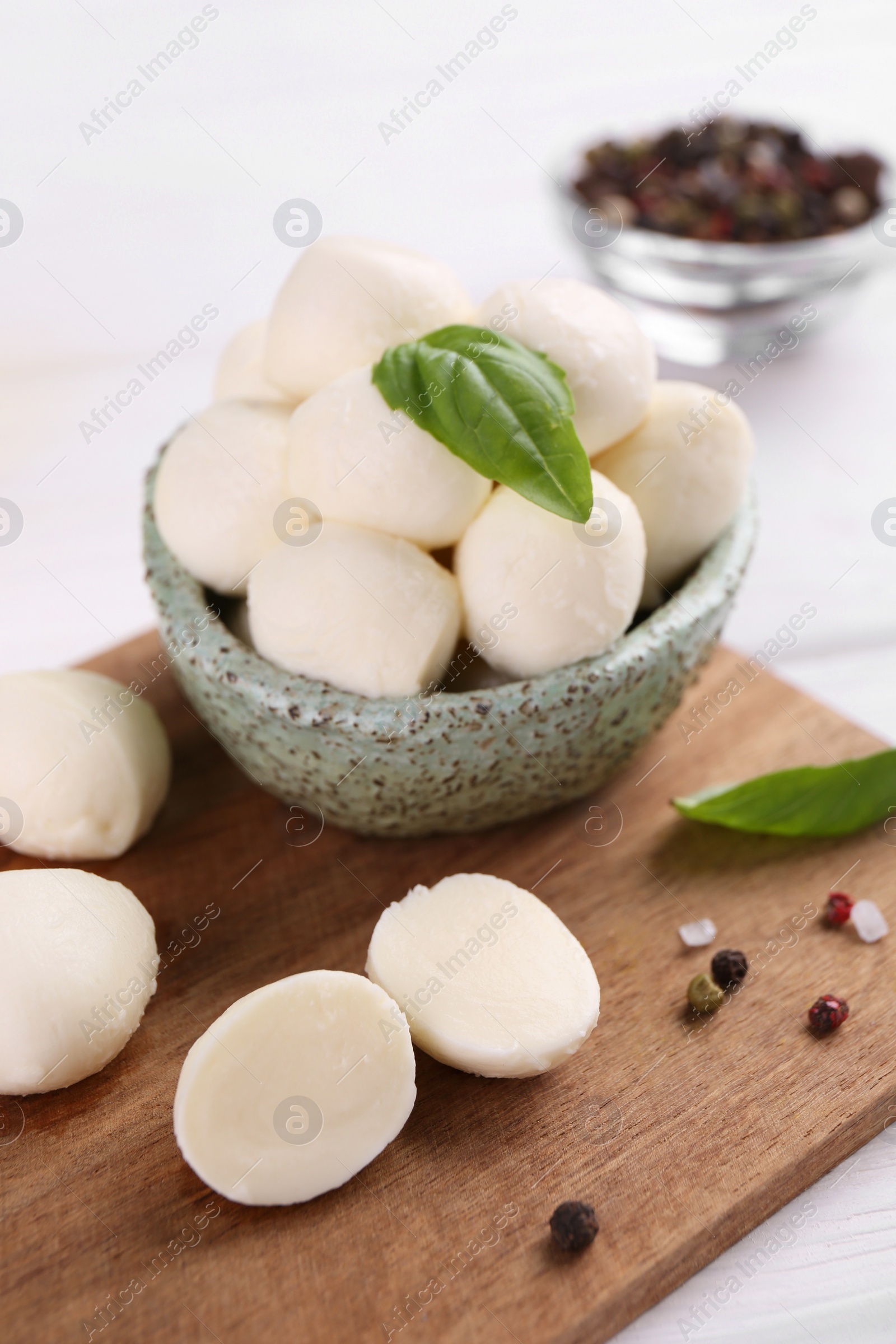 Photo of Tasty mozzarella balls, basil leaves and spices on white wooden table, closeup