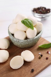 Tasty mozzarella balls, basil leaves and spices on white wooden table, closeup