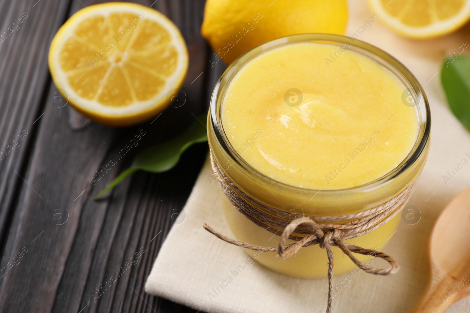 Photo of Delicious lemon curd in bowl, fresh citrus fruits and spoon on wooden table, closeup