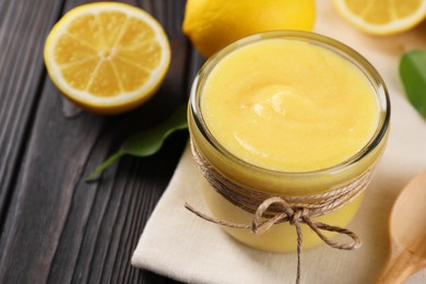 Photo of Delicious lemon curd in bowl, fresh citrus fruits and spoon on wooden table, closeup