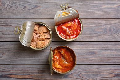 Tin cans with fish on wooden table, flat lay