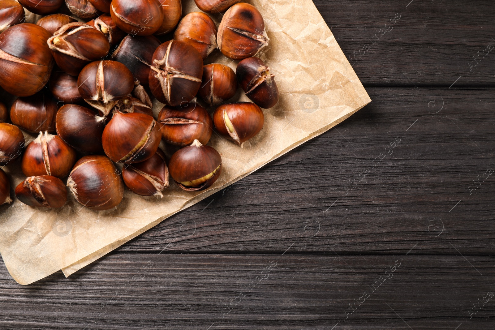 Photo of Tasty roasted edible chestnuts on black wooden table, top view. Space for text