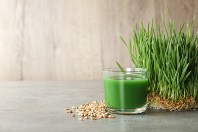Photo of Glass of juice, sprouted wheat grass and grains on table. Space for text