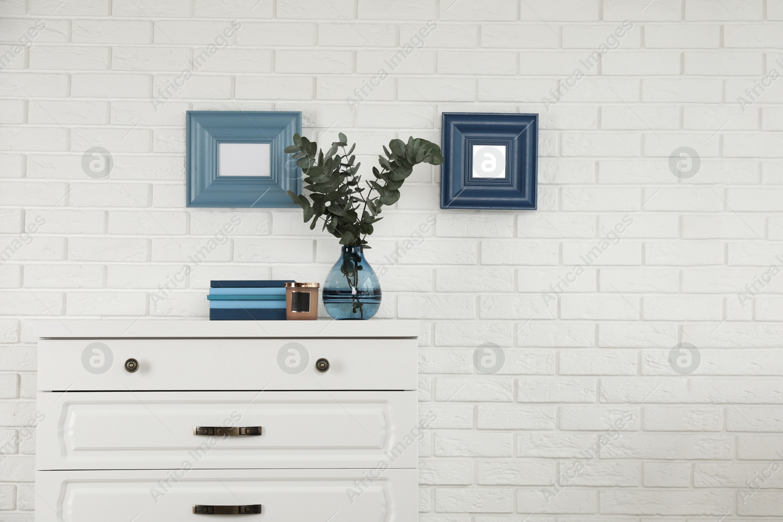 Photo of Modern chest of drawers with decor near white brick wall