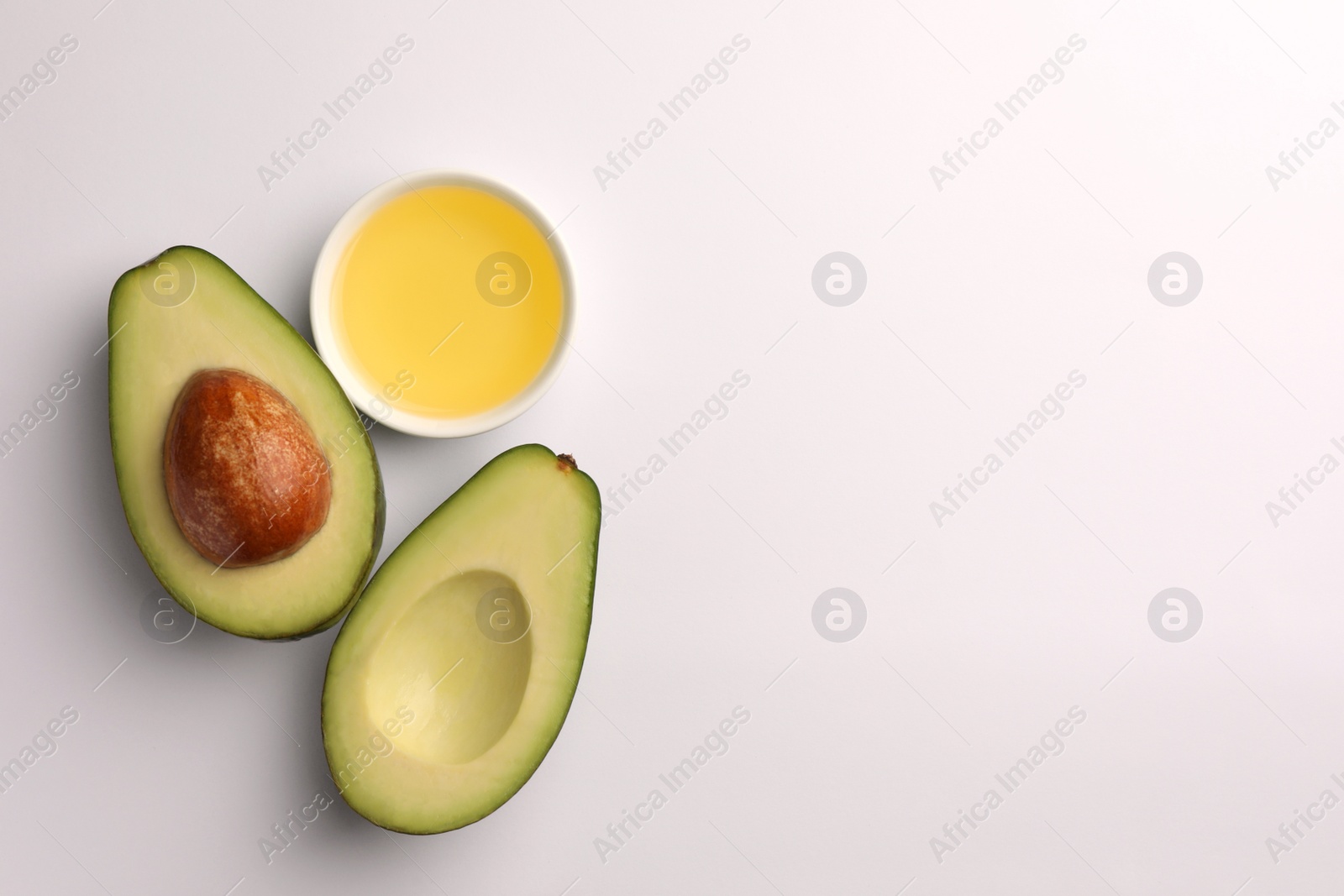 Photo of Cooking oil in bowl and fresh avocados on white background, flat lay. Space for text