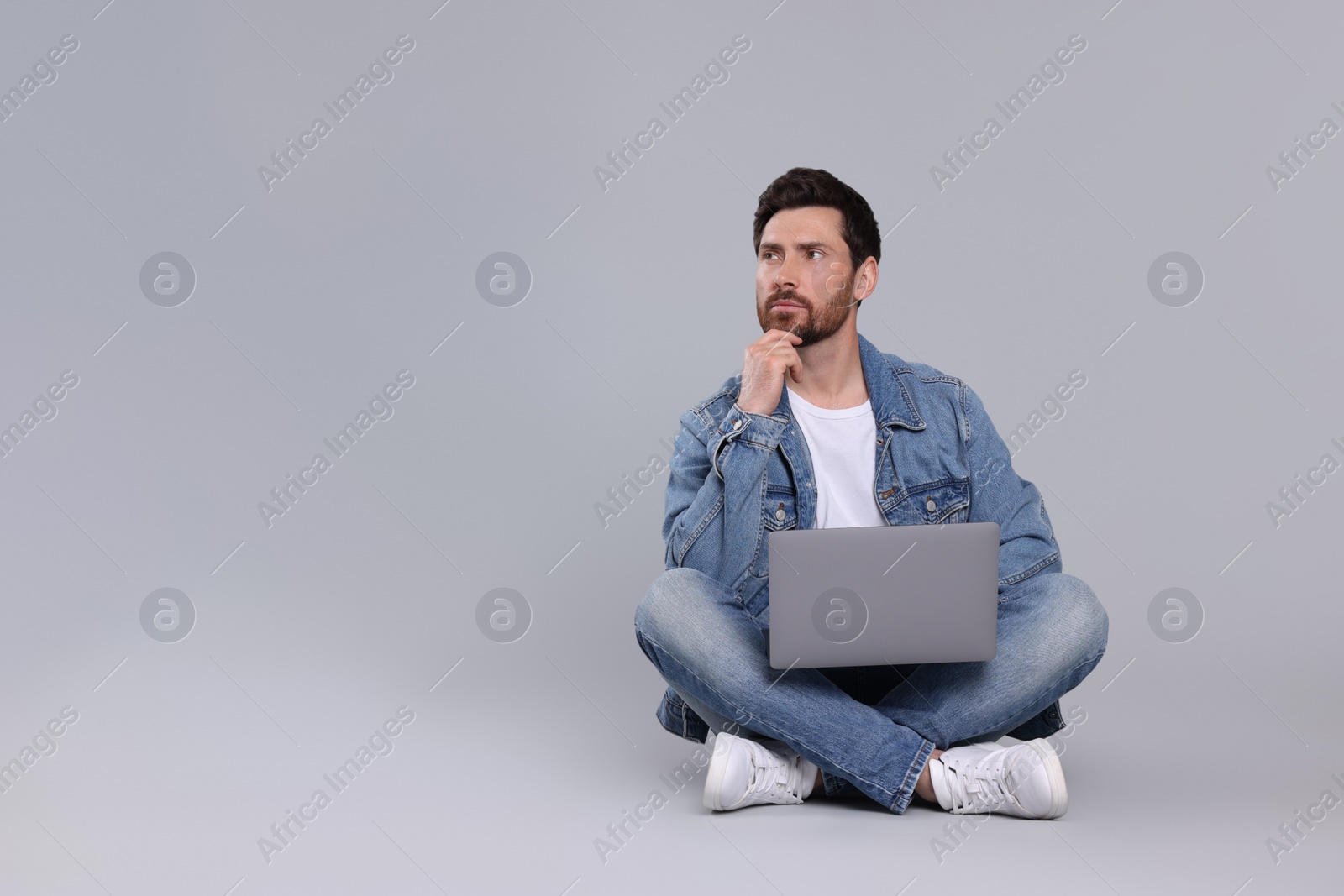 Photo of Confused man with laptop on light grey background. Space for text