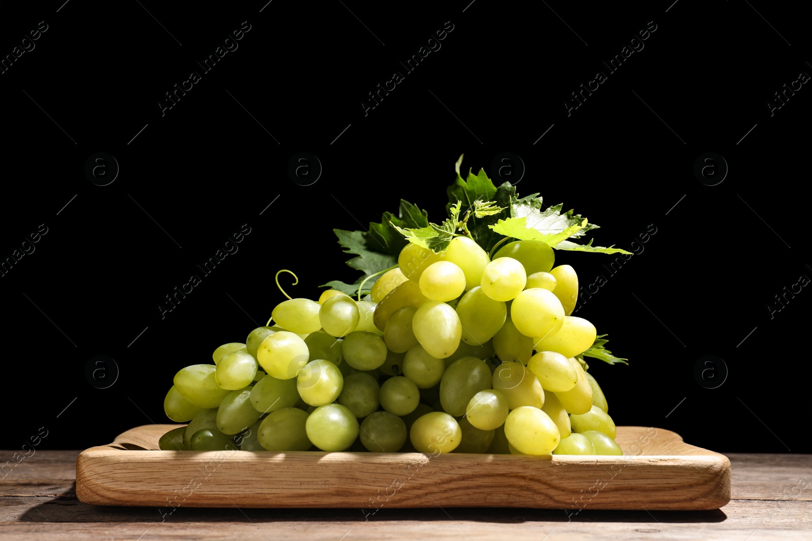 Photo of Fresh ripe juicy grapes on wooden table against black background