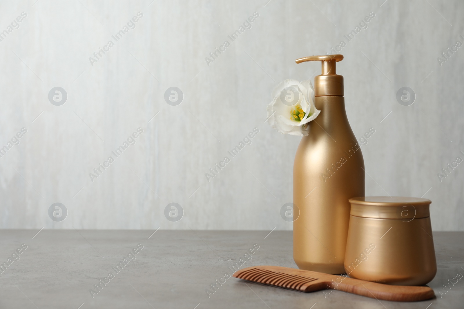 Photo of Different hair products, flower and wooden comb on grey table. Space for text