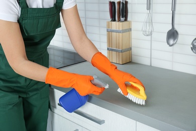 Photo of Female janitor cleaning kitchen counter with brush, closeup