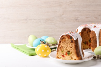 Photo of Piece of glazed Easter cake with sprinkles and painted eggs on white wooden table, space for text