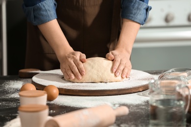 Photo of Woman kneading dough on board covered with flour in kitchen