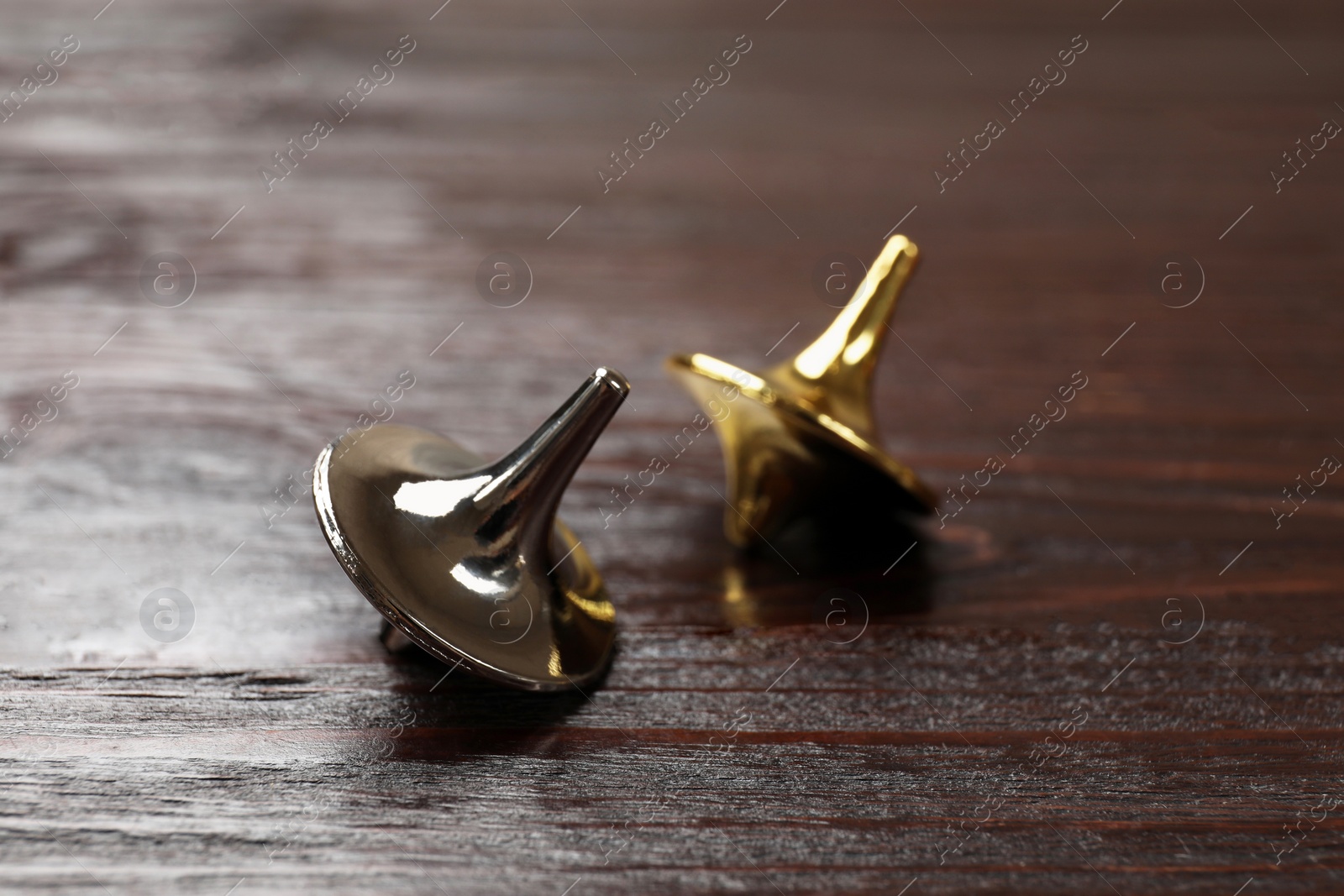 Photo of Two metal spinning tops on wooden table, closeup