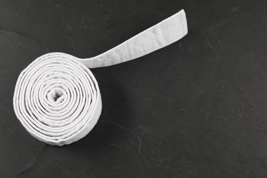 Photo of Rolled white karate belt on gray background, top view. Space for text